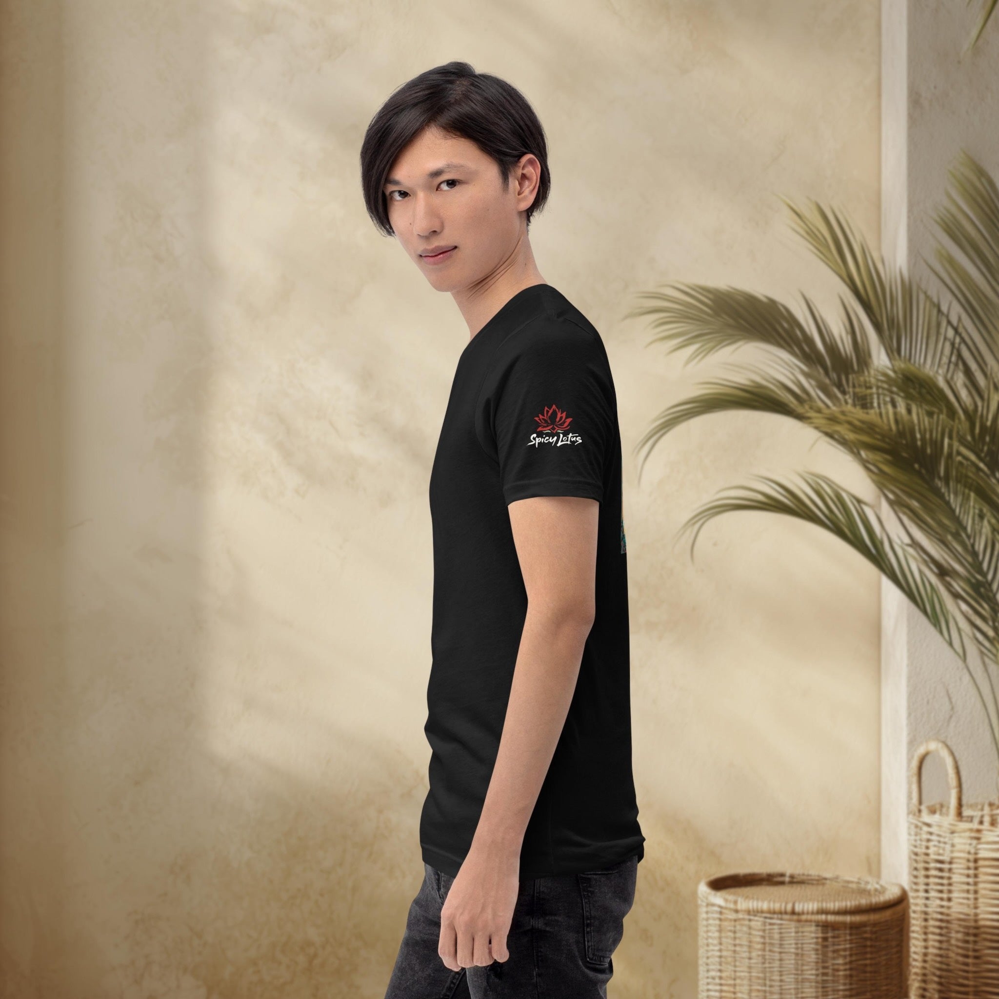 Person wearing a black t-shirt with a logo against a textured wall with plant decor