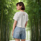 Woman wearing a white t-shirt with a logo and denim shorts standing in a bamboo forest