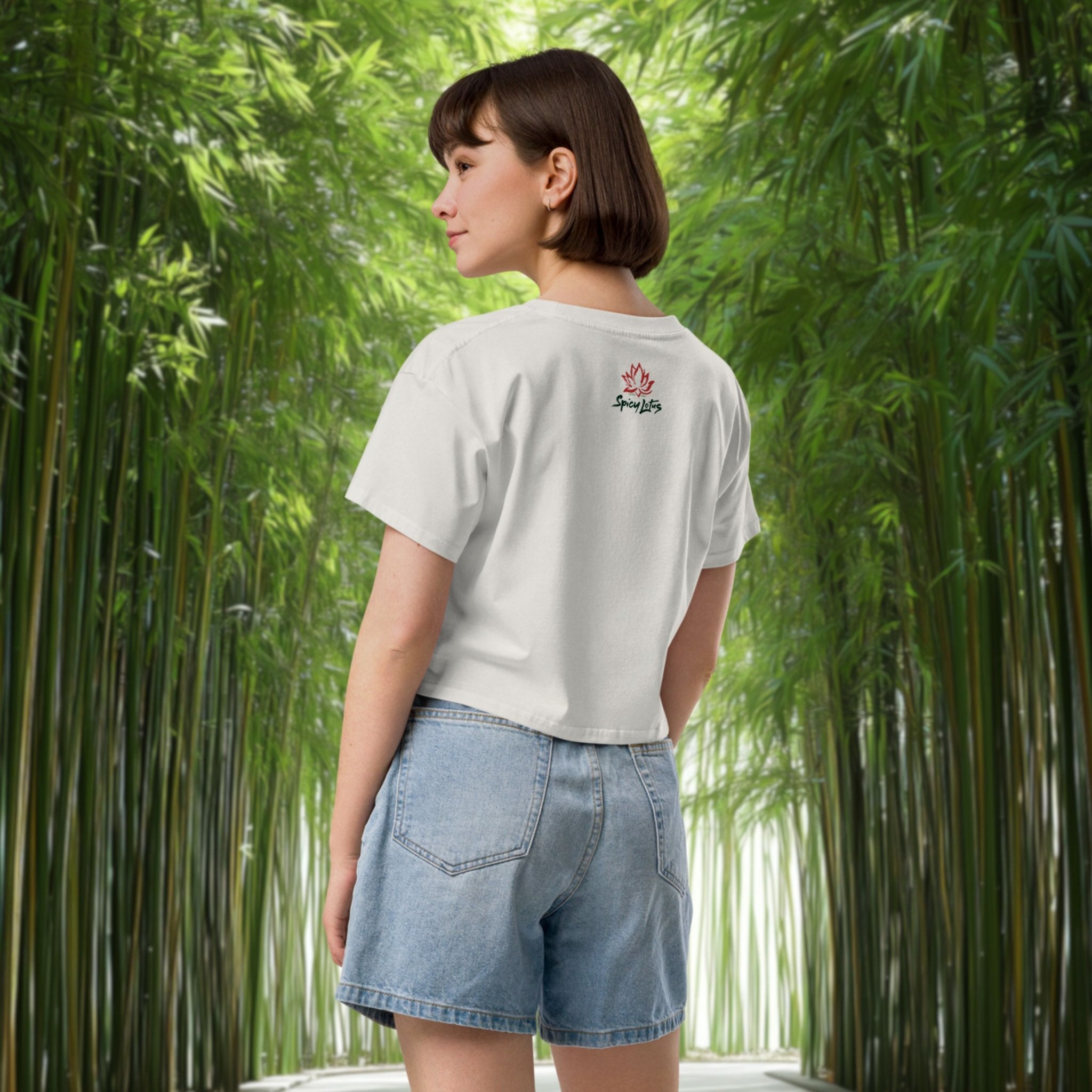 Woman wearing a white t-shirt with a logo and denim shorts standing in a bamboo forest