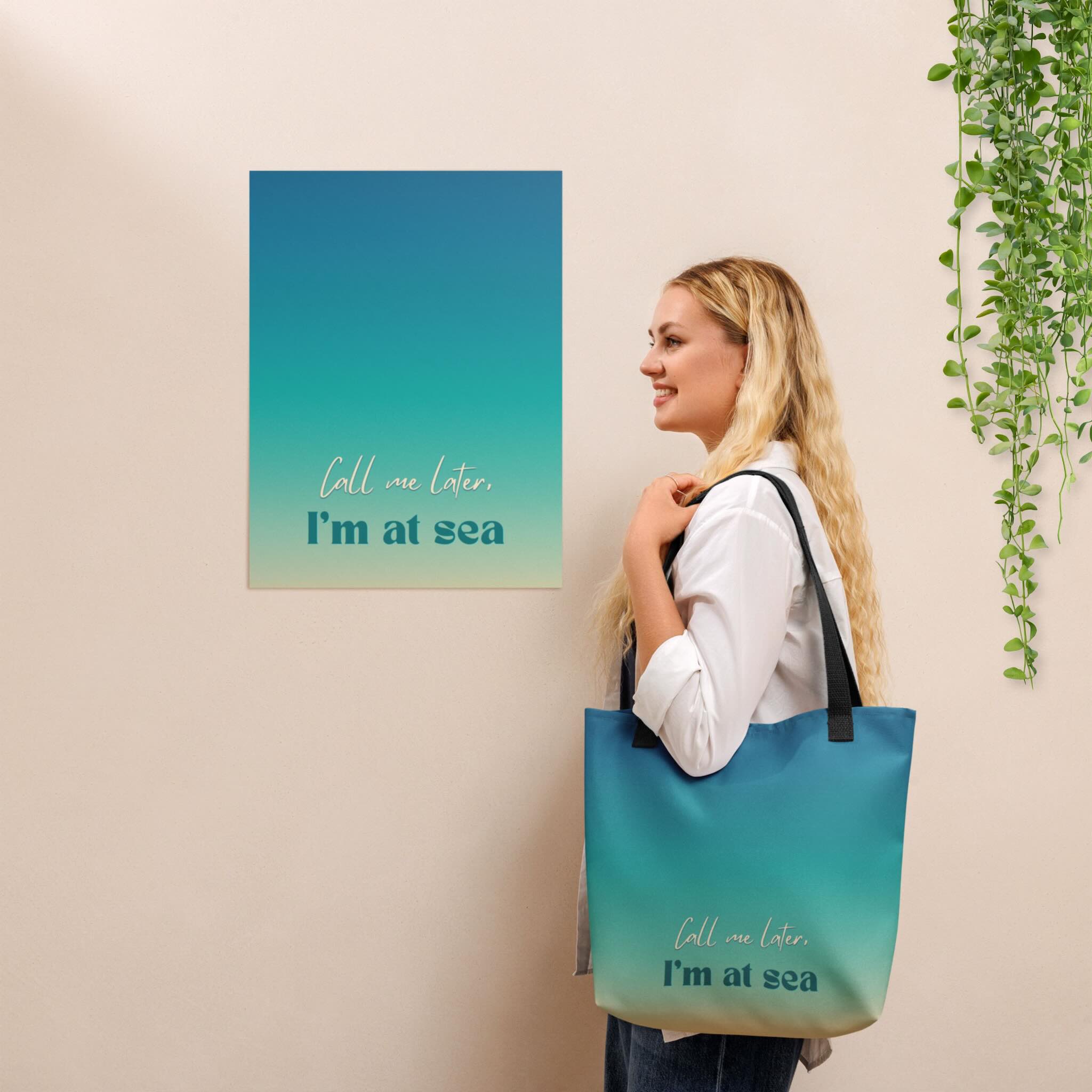 Woman holding a blue tote bag with 'Call me later, I'm at sea' text next to a matching wall art piece.