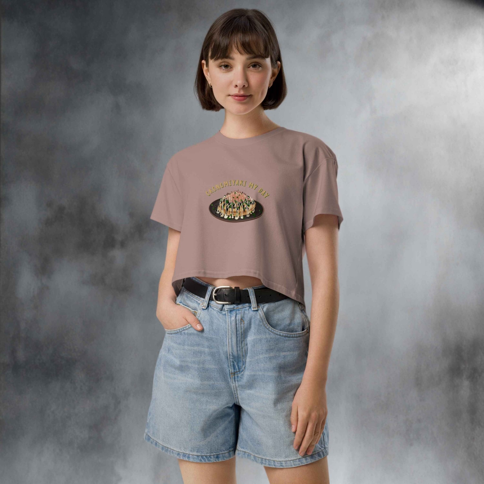 Person wearing a beige t-shirt with a graphic design  of japanese pancake and denim shorts in a studio setting
