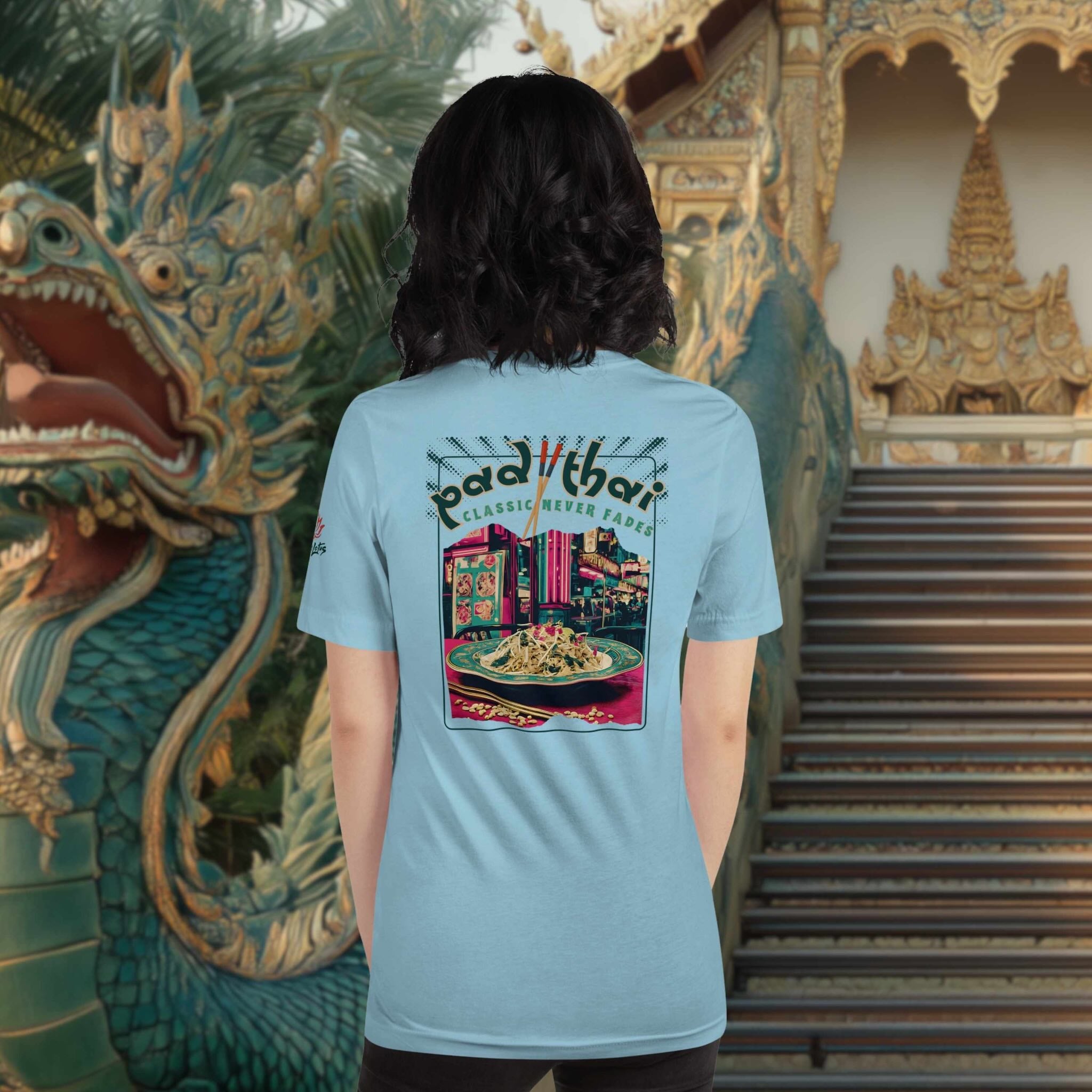 Person wearing a light blue t-shirt with a colorful Pad Thai graphic design in front of a Thai temple with a dragon statue.