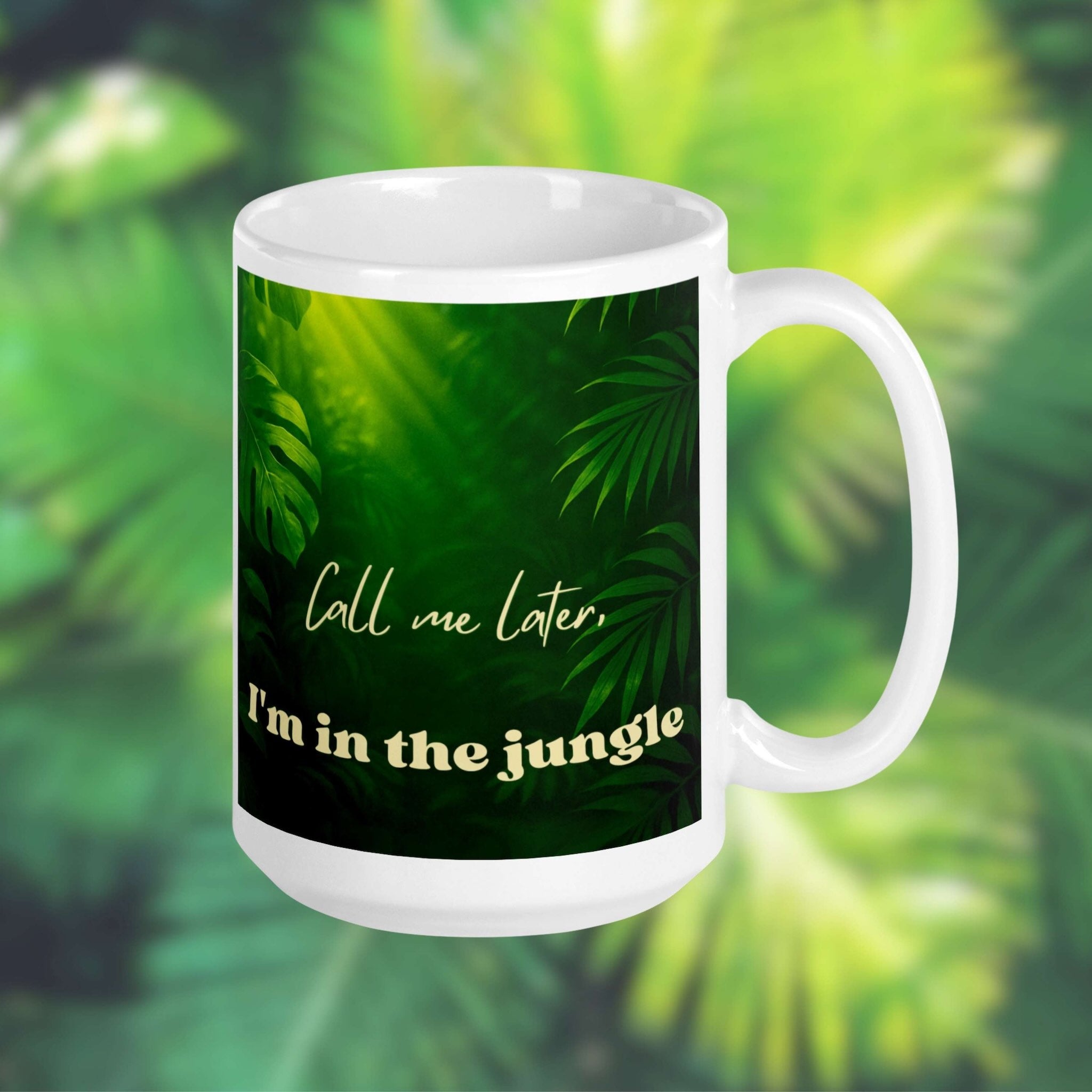 White 15 oz mug with green leafy pattern and text 'Call me later, I'm in the jungle' on a blurred green foliage background.