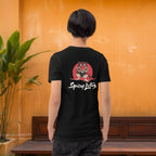 Person wearing a black t-shirt with 'Spicy Lotus' tiger design, standing against an orange wall.