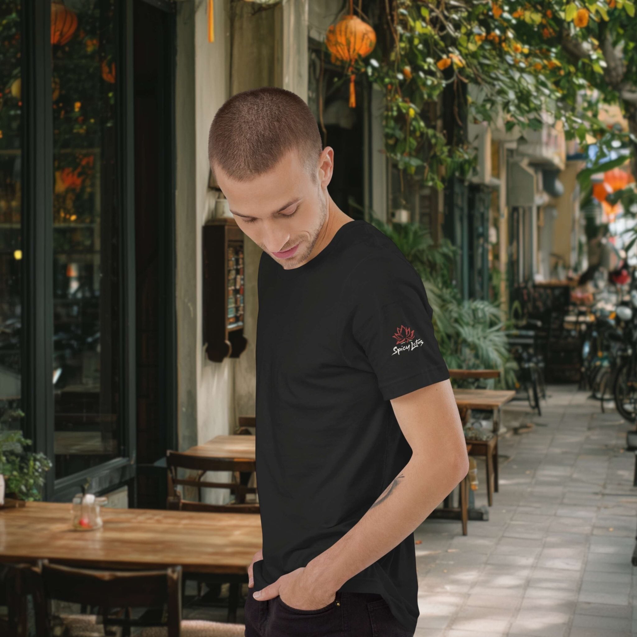 Man wearing a black t-shirt with a logo on a street with tables and chairs.