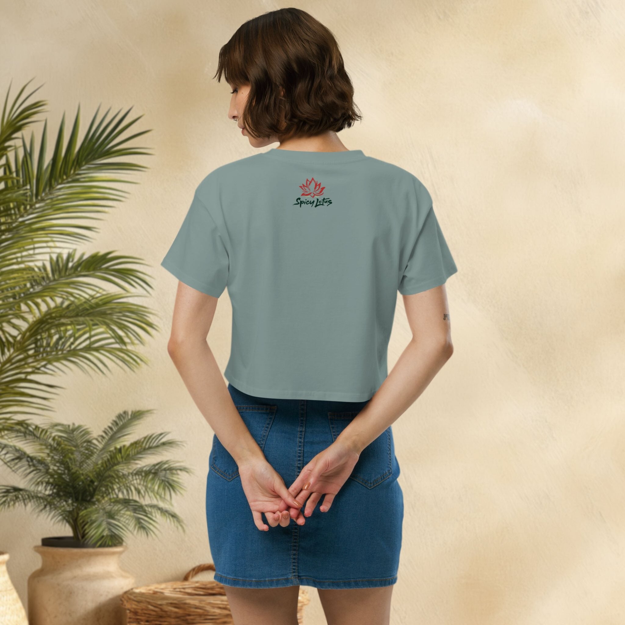 Person wearing a light bluecrop top with a logo on the back, standing in front of a plant.
