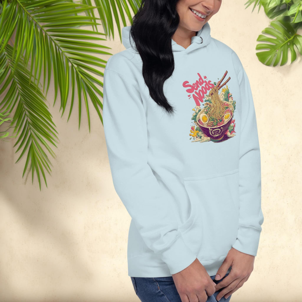 Person wearing a light blue hoodie with a colorful graphic design of japanese ramen with the pun 'Send Noods' on a beige background with green leaves.