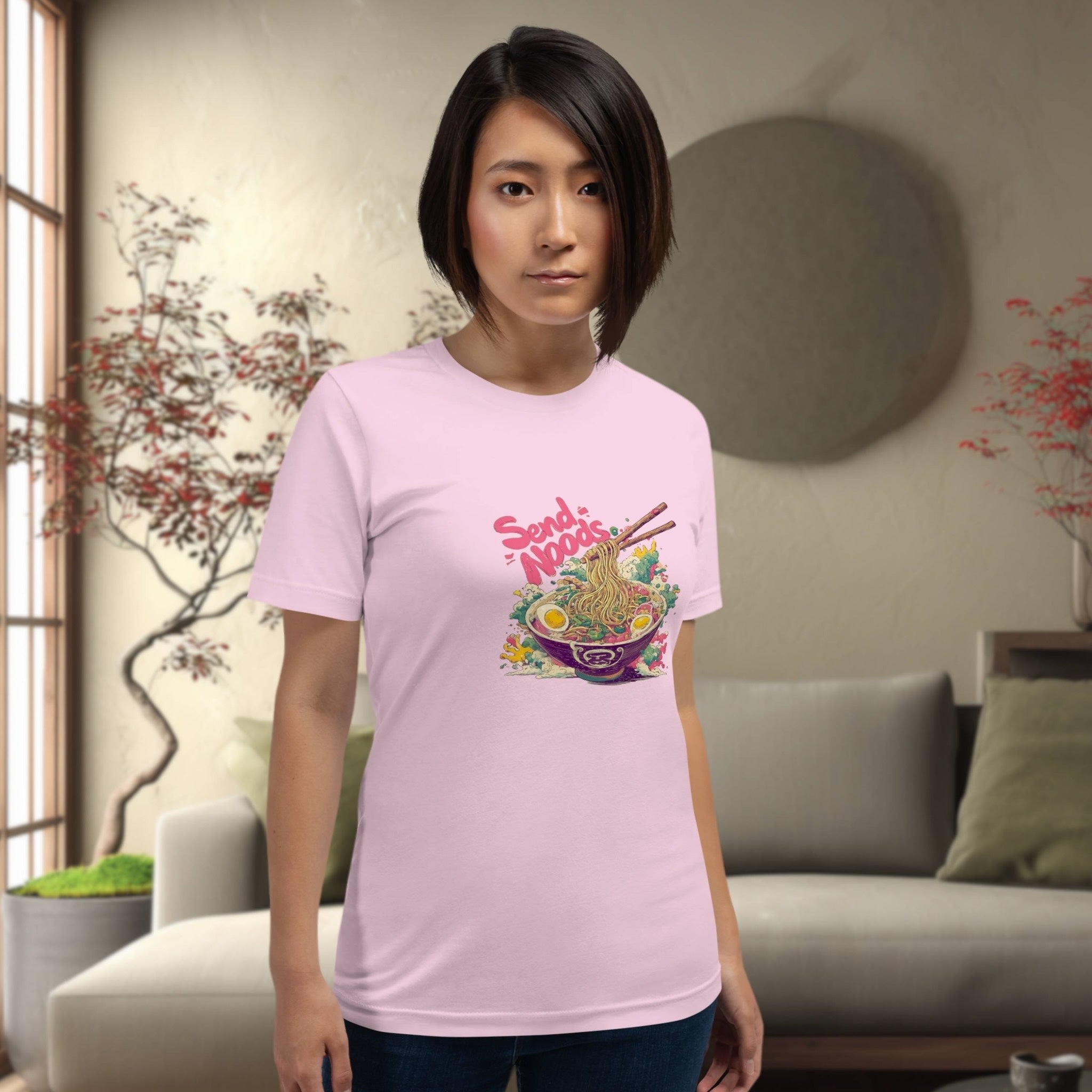 Person wearing a pink t-shirt with a colorful graphic design of japanese ramen 'send noods' in a living room setting