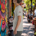 Person wearing a gray t-shirt with colorful laksa design on a street scene