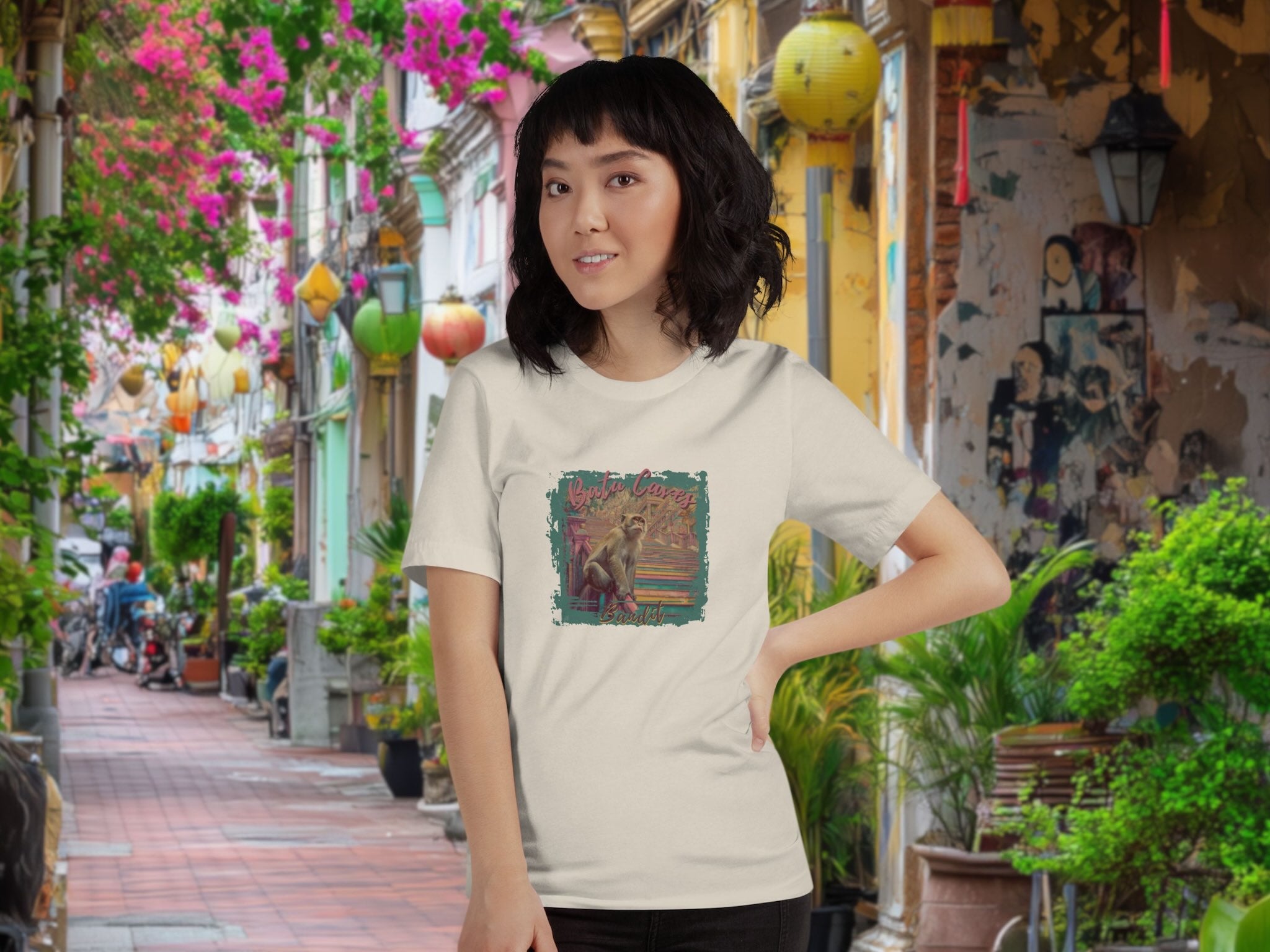 Woman wearing a t-shirt with a colorful graphic design of Batu Caves Bandit monkey front print in an outdoor setting with plants and decorations.