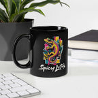 Black mug with colorful gecko design and 'Spicy Lotus' text on a desk with books and plant.