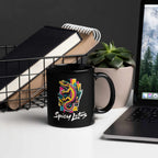 Black mug with colorful gecko design and 'Spicy Lotus' text on a desk with laptop and books.