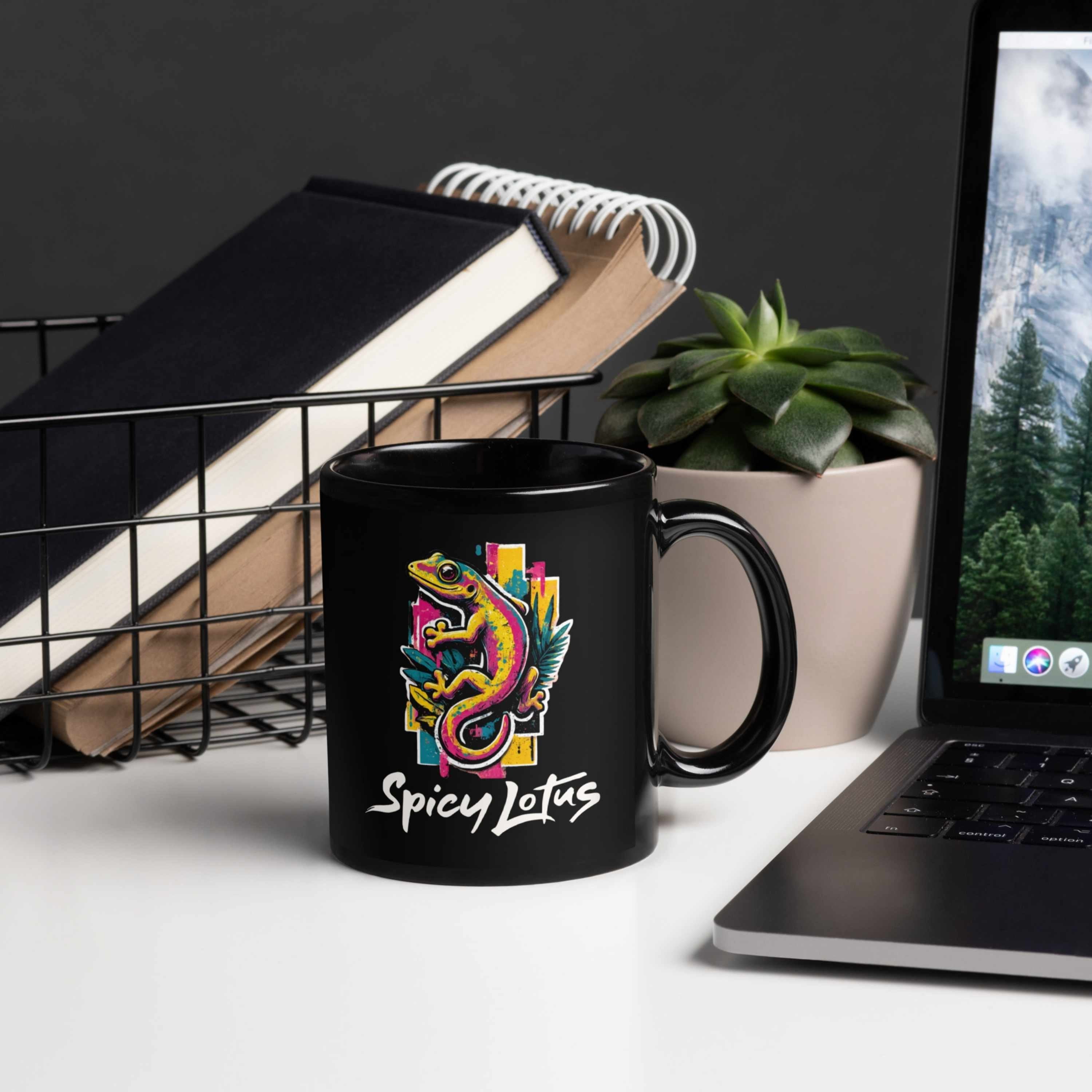 Black mug with colorful gecko design and 'Spicy Lotus' text on a desk with laptop and books.