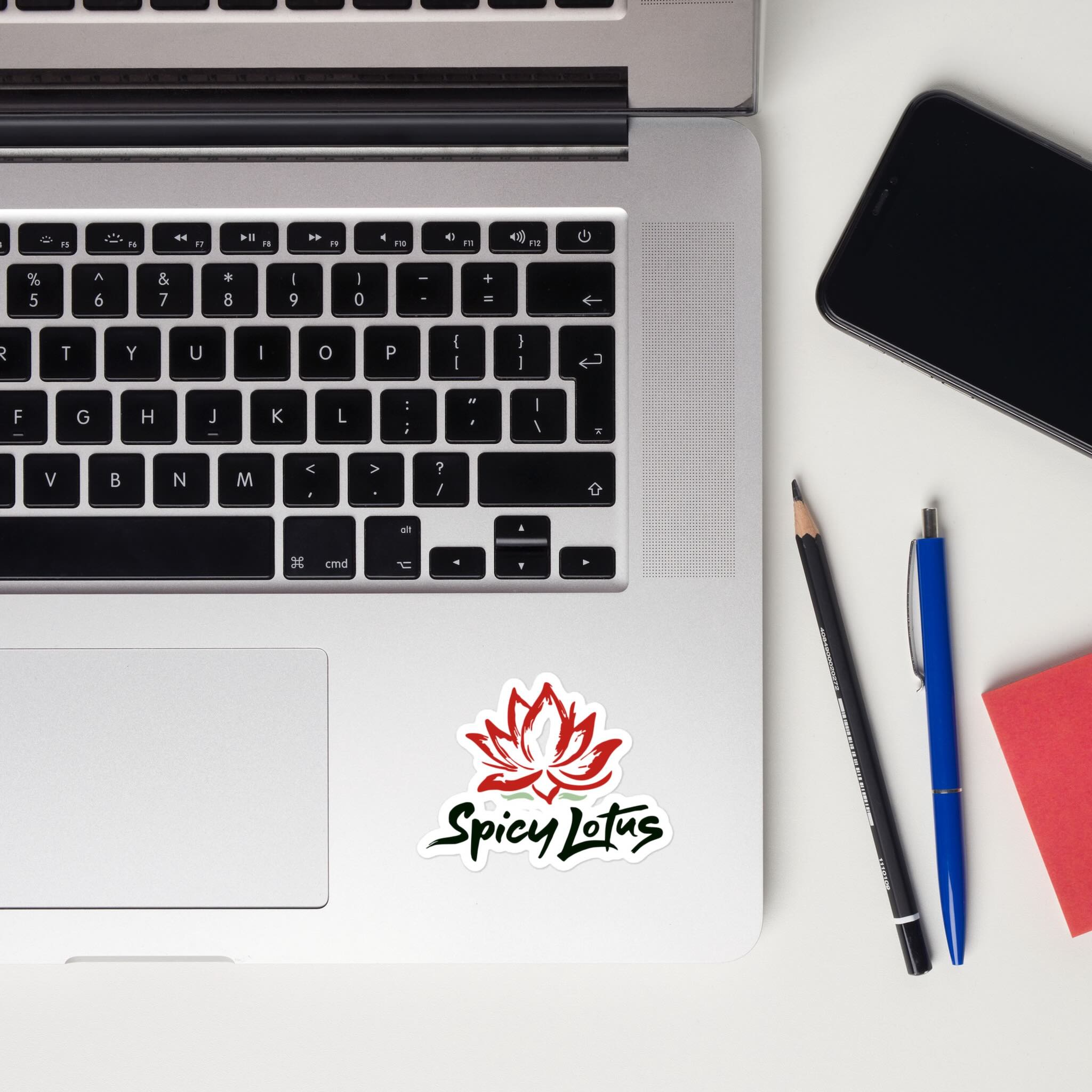 Laptop with Spicy Lotus logo kiss cut sticker, smartphone, pencil, and pen on a white surface