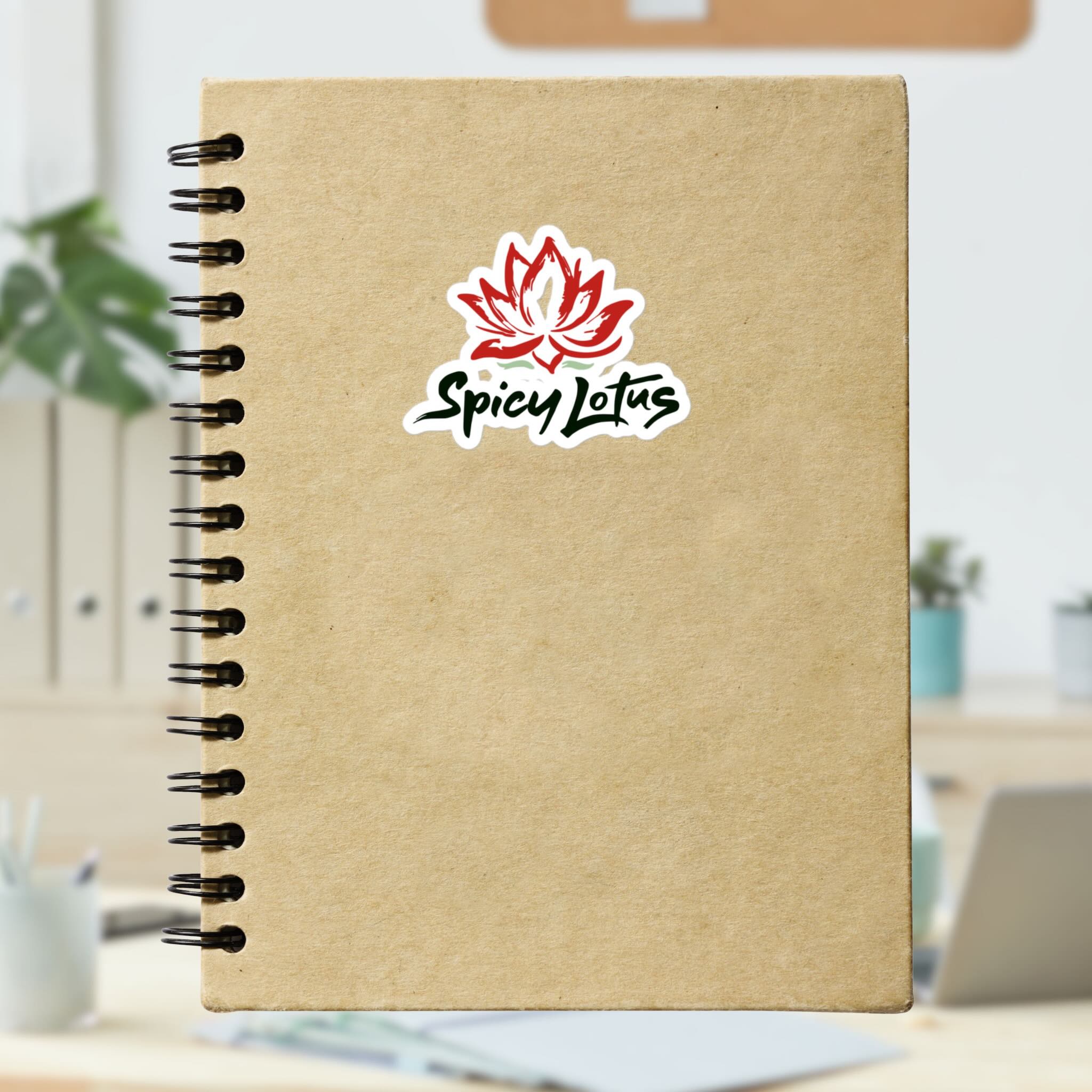 Brown notebook with Spicy Lotus logo kiss cut sticker with lotus flower on a blurred indoor background