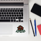 Laptop with Spicy Lotus sticker with lotus flower and brand name in white font on a notebook next to a phone, pencil, and pen.