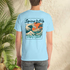 Person wearing a light blue t-shirt with 'Spicy Lotus Surf Club' design, standing against a textured wall with greenery.