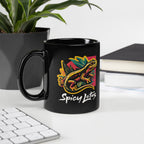 Black mug with colorful gecko design and 'Spicy Lotus' text on a desk with a plant and books in the background.