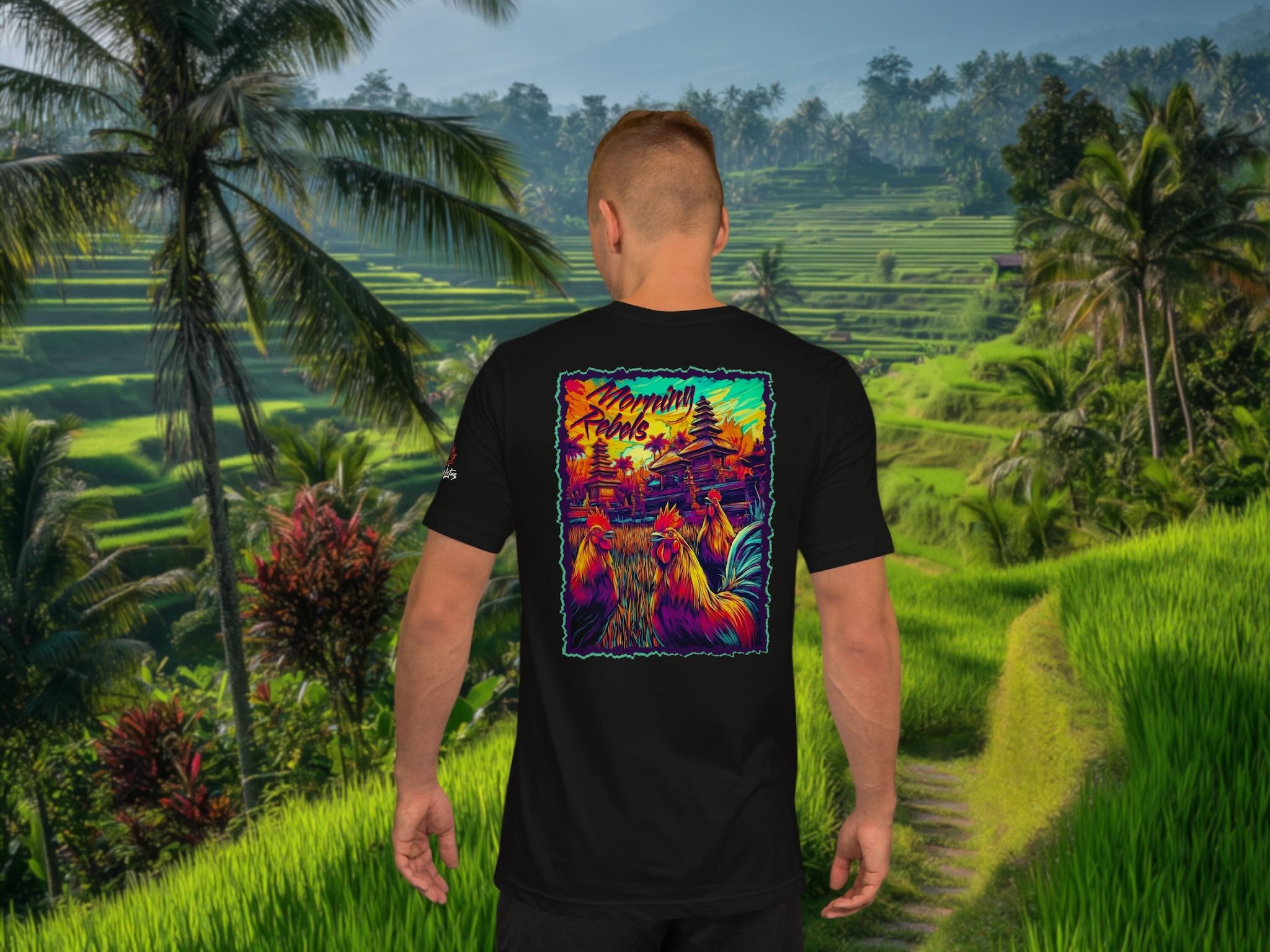 Person wearing a black t-shirt with a colorful rooster graphic design in a tropical setting with rice fields and palm trees.