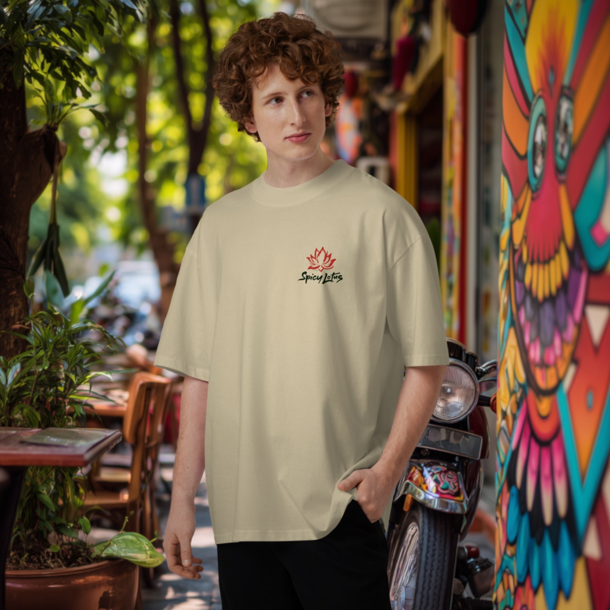 Man wearing a beigeoversized high neck  t-shirt with a  chest logo, standing in an outdoor setting with colorful graffiti.