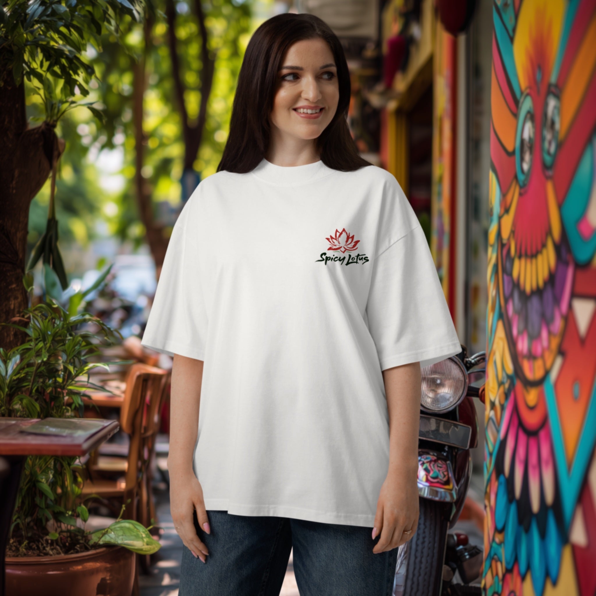 Woman wearing a big organic white t-shirt with a chest logo with lotus flower and brand name in an outdoor setting with lush green and graffiti wall