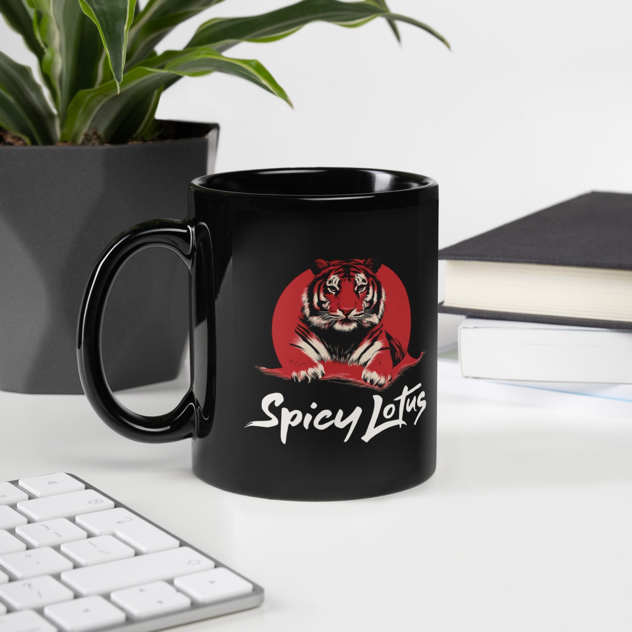 Black mug with a tiger design and 'Spicy Lotus' text on a desk with a plant and books in the background.
