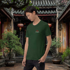 Person wearing a green t-shirt with a logo in a japanese outdoor setting with traditional architecture and plants.