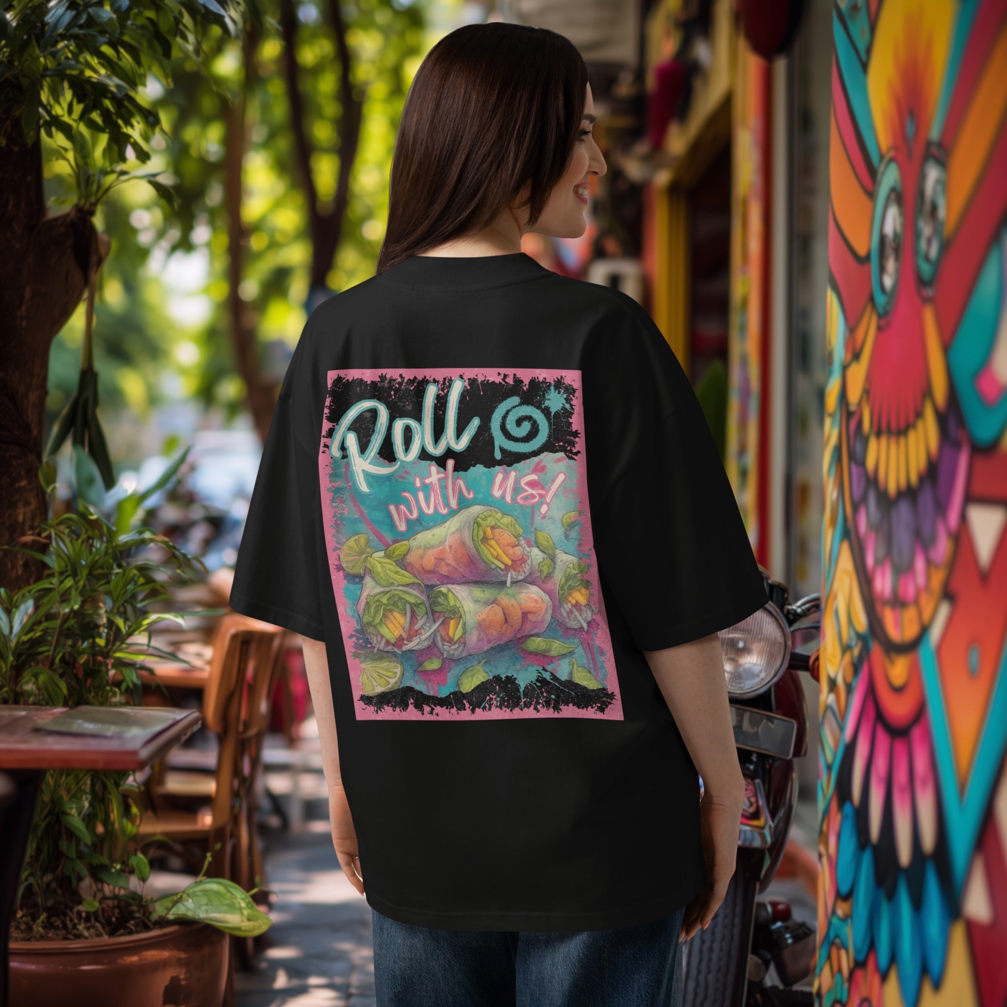 Woman wearing a black oversized  t-shirt with colorful graphic 'Roll with us' summer rolls design in an outdoor setting