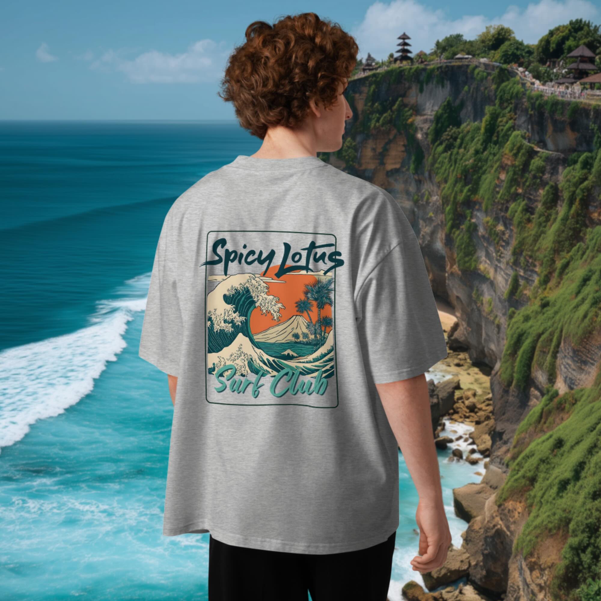Person wearing a  grey oversized 'Spicy Lotus Surf Club' t-shirt with a scenic ocean view in the background in Uluwatu, Bali