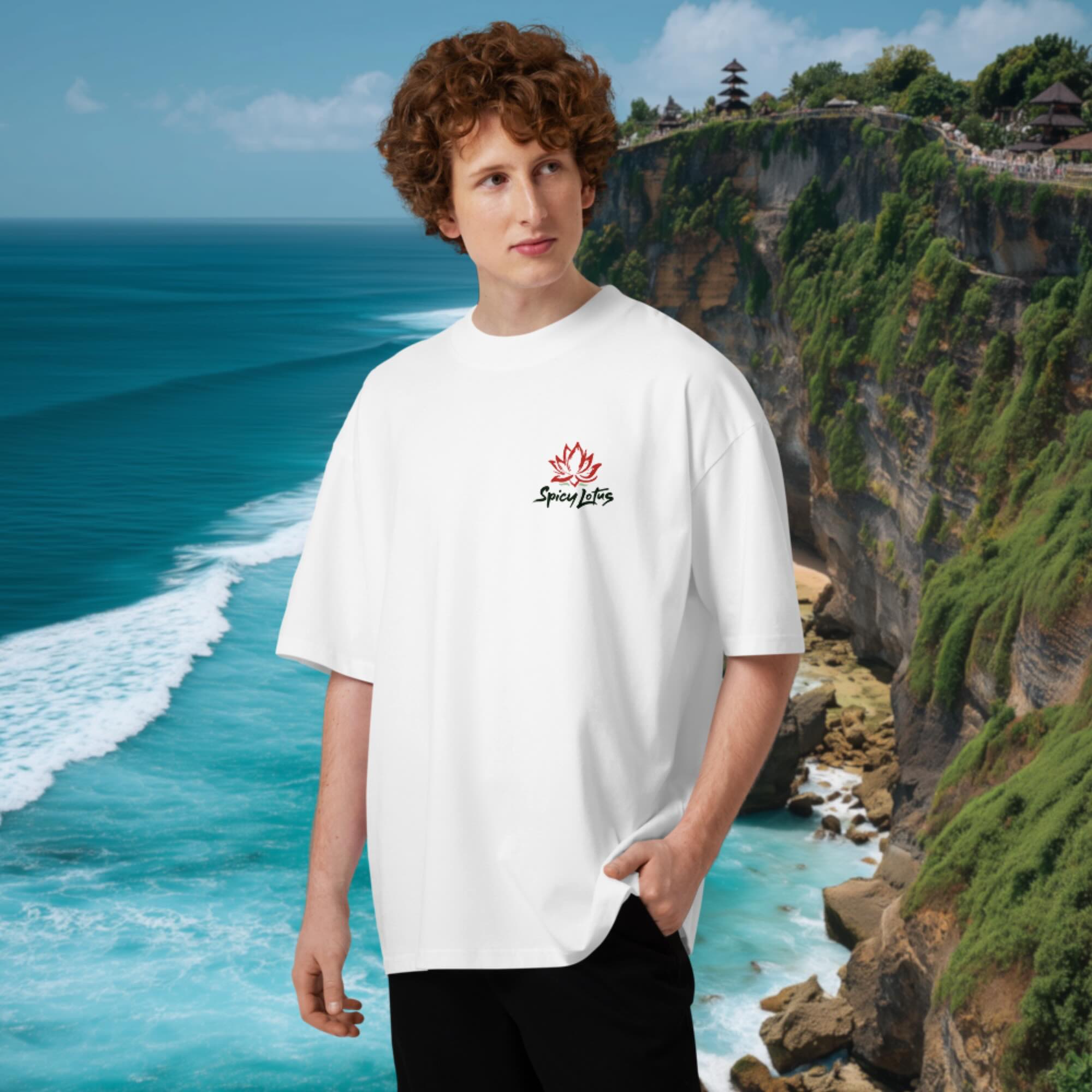 Male model wearing a oversized white t-shirt with a chest logo in front of a scenic ocean and cliff backdrop in Uluwatu, Bali.