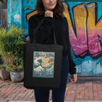 Woman holding a black tote bag with 'Spicy Lotus Surf Club' design in front of a colorful mural.