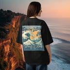 Woman wearing a black t-shirt with a graphic design of a wave and text 'Spicy Lotus Surf Club', standing on a cliff overlooking the ocean.