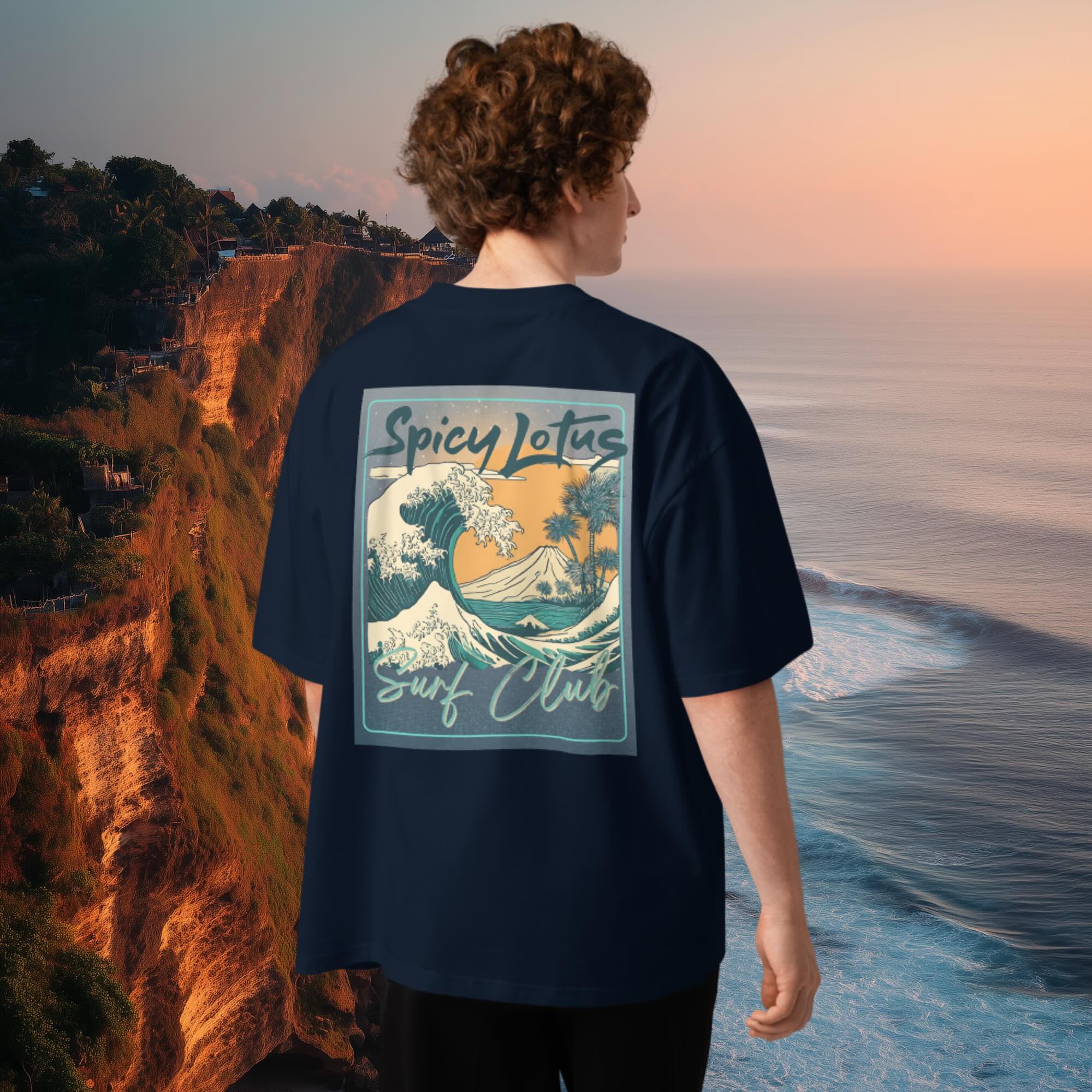 Male model wearing a navy blue t-shirt with 'Spicy Lotus Surf Club' design, standing on a cliff overlooking the ocean.