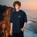 Male model wearing a navy blue 100 % cotton oversized Stanley tee with a Spicy Lotus chest logo standing on a beach with cliffs of Uluwatu, Bali  in the background 