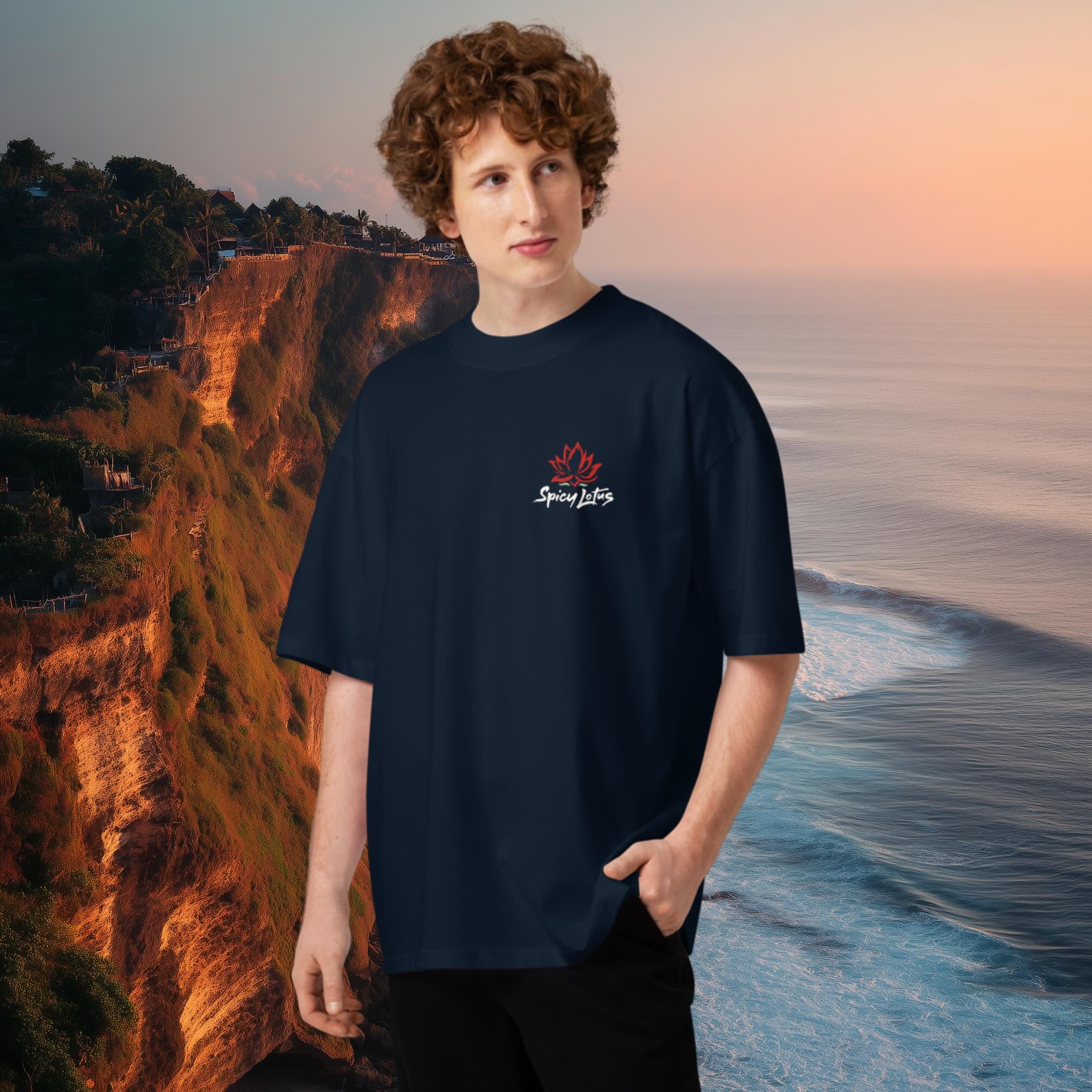 Male model wearing a navy blue 100 % cotton oversized Stanley tee with a Spicy Lotus chest logo standing on a beach with cliffs of Uluwatu, Bali  in the background 
