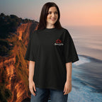 Woman wearing a black high-neck ribbed collar and dropped shoulders oversized tee  with a logo in front of a scenic background in Uluwatu, Bali.
