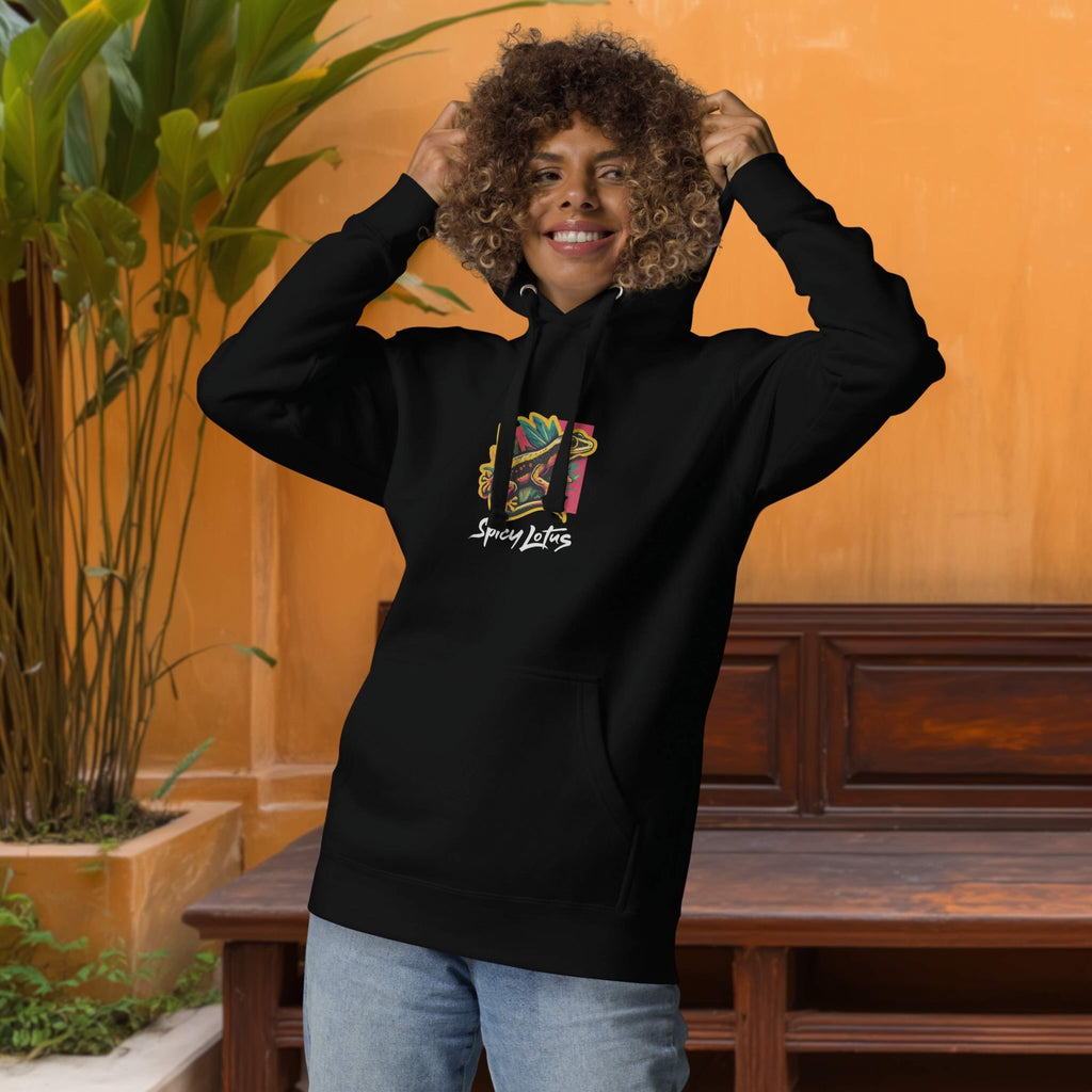 Person wearing a black hoodie with colorful design of geckos and tbrand name 'Spicy Lotus', standing against an orange wall with a wooden bench and plant.