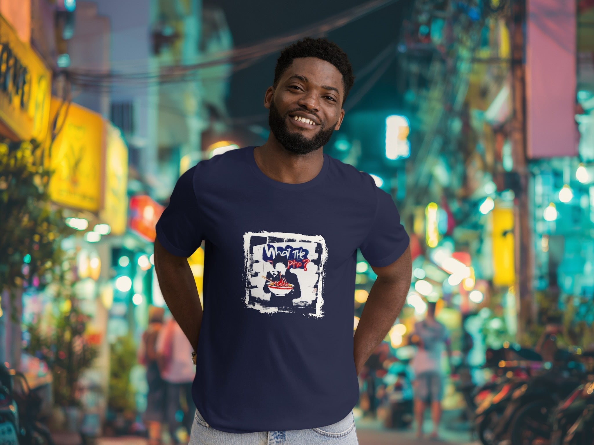 Man wearing a navy blue t-shirt with a graphic designof vietnamese pho in an urban setting with colorful lights.