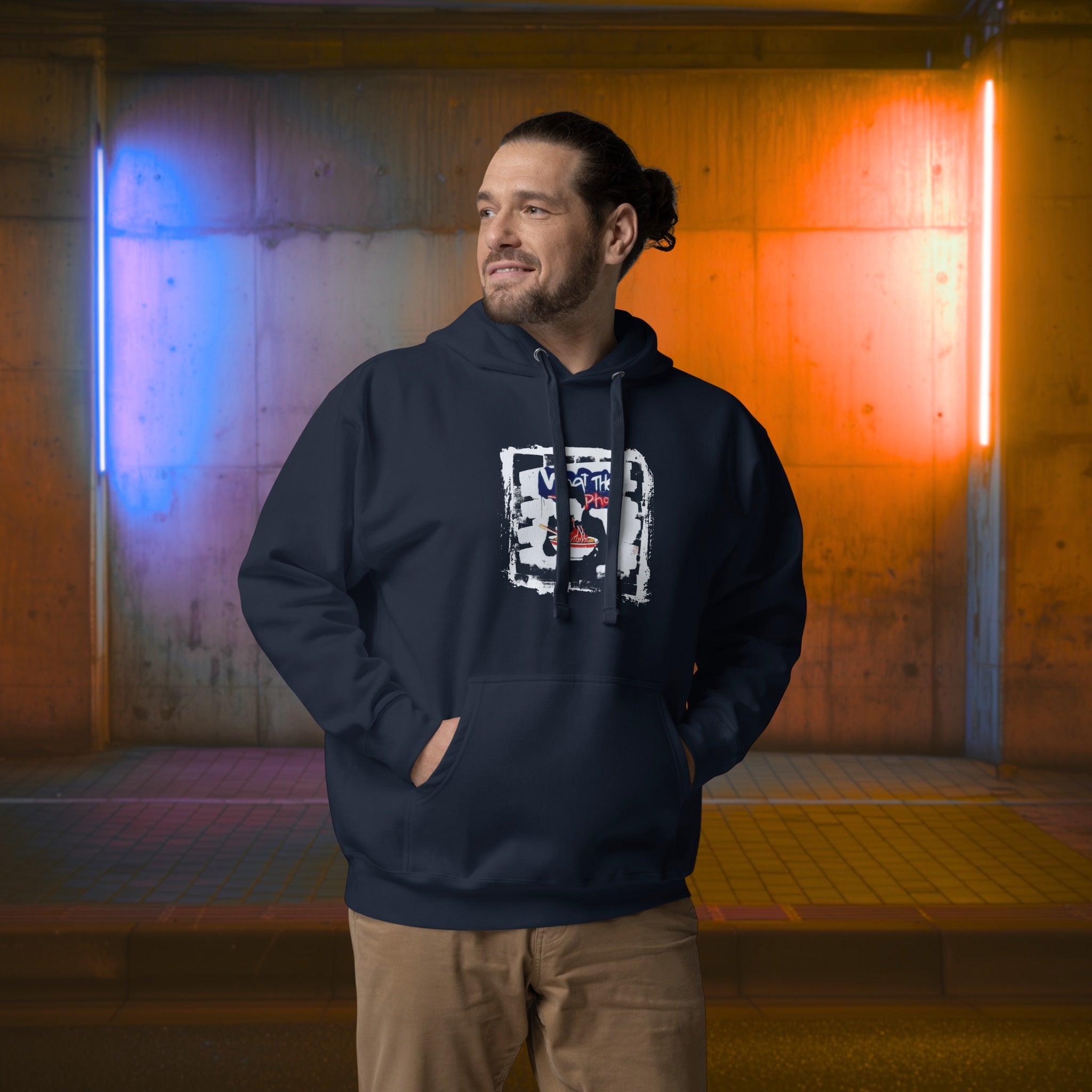 Man wearing a dark hoodie with a graphic design  of graffiti style 'what the pho' in front of a colorful, abstract wall. 