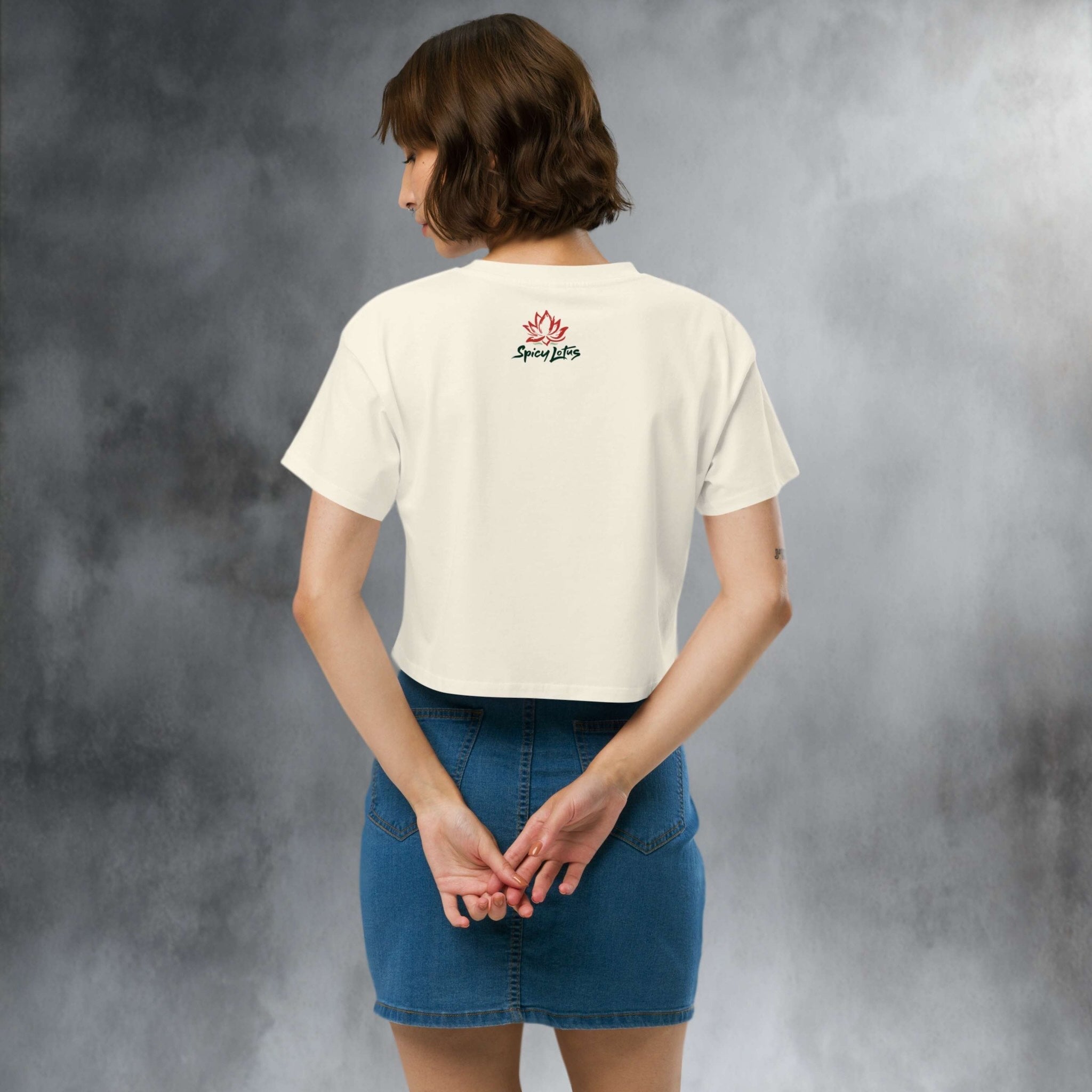 Person wearing a white crop top t-shirt with a logo on the back, standing in a studio setting.