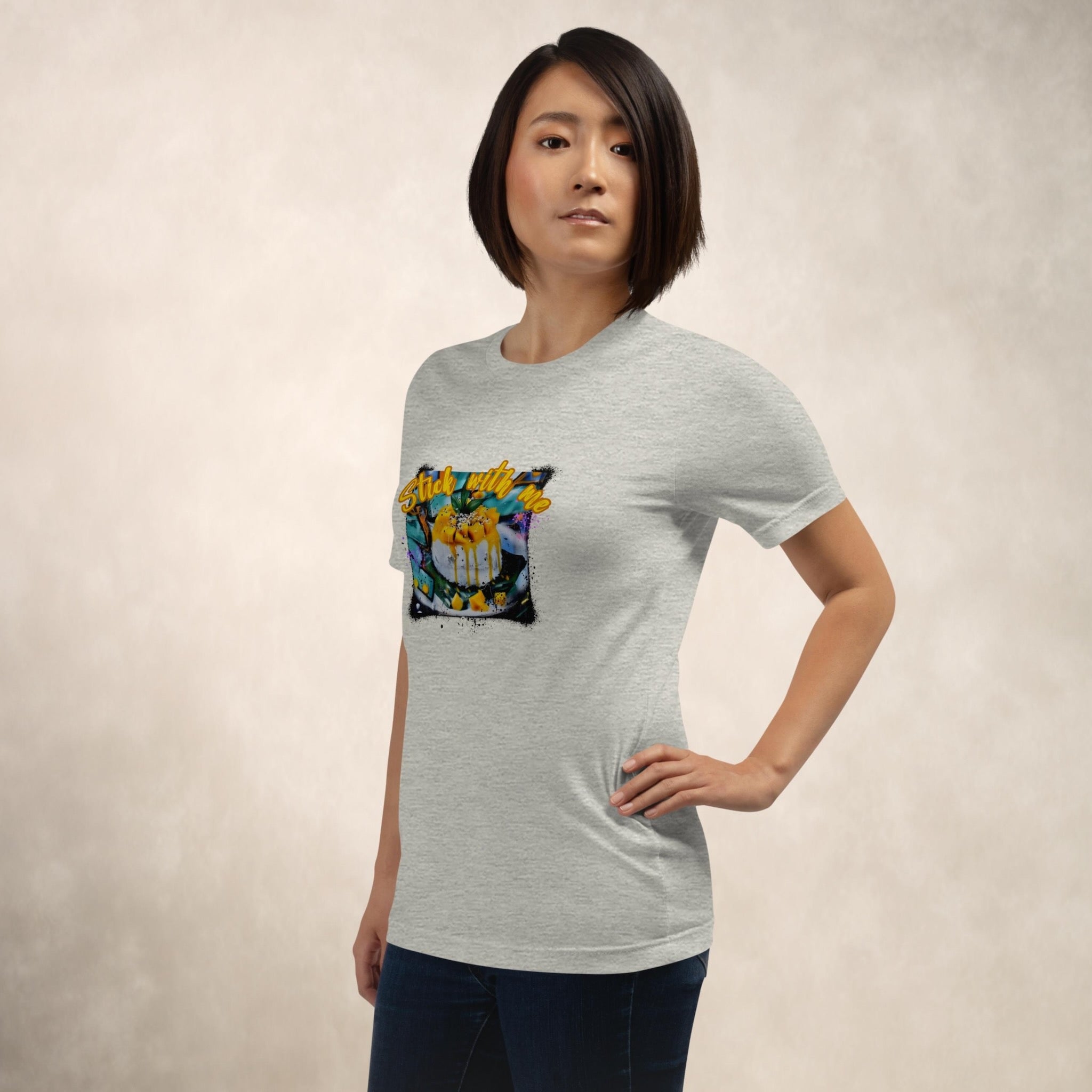 Person wearing a gray t-shirt with a colorful Stick With Me mango sticky rice street art t-shirt front print on a beige background