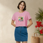 Woman wearing a pink t-shirt with a graphic design of cute and colorful mochis, standing against a beige wall with a plant and basket in the background.