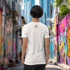 Person wearing a white t-shirt with a logo in an urban alleyway with colorful graffiti.
