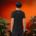 Person wearing a black t-shirt with a logo on the back, standing in front of an orange wall with plants.
