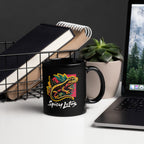 Black mug with colorful design and text 'Optimistic Nihilism' on a desk with laptop and books.