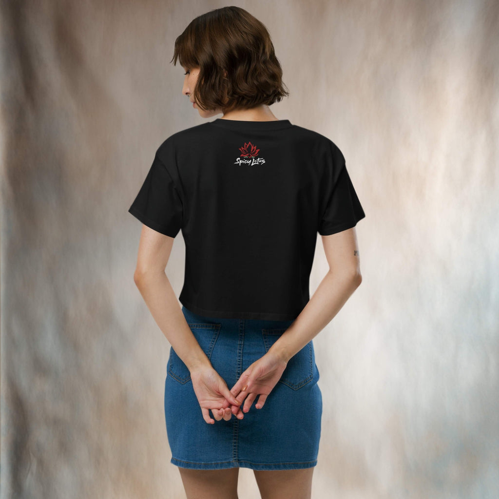 Person wearing a black crop tee with a logo on the back, standing in front of a neutral backdrop.