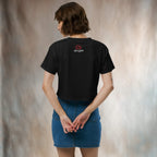 Person wearing a black crop tee with a logo on the back, standing in front of a neutral backdrop.