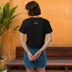 Person wearing a black t-shirt with a logo on the back, standing in front of an orange wall.