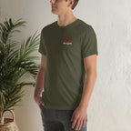 Man wearing green Bella+Canvas 3001 unisex tee with chest logo in front of wall and plant